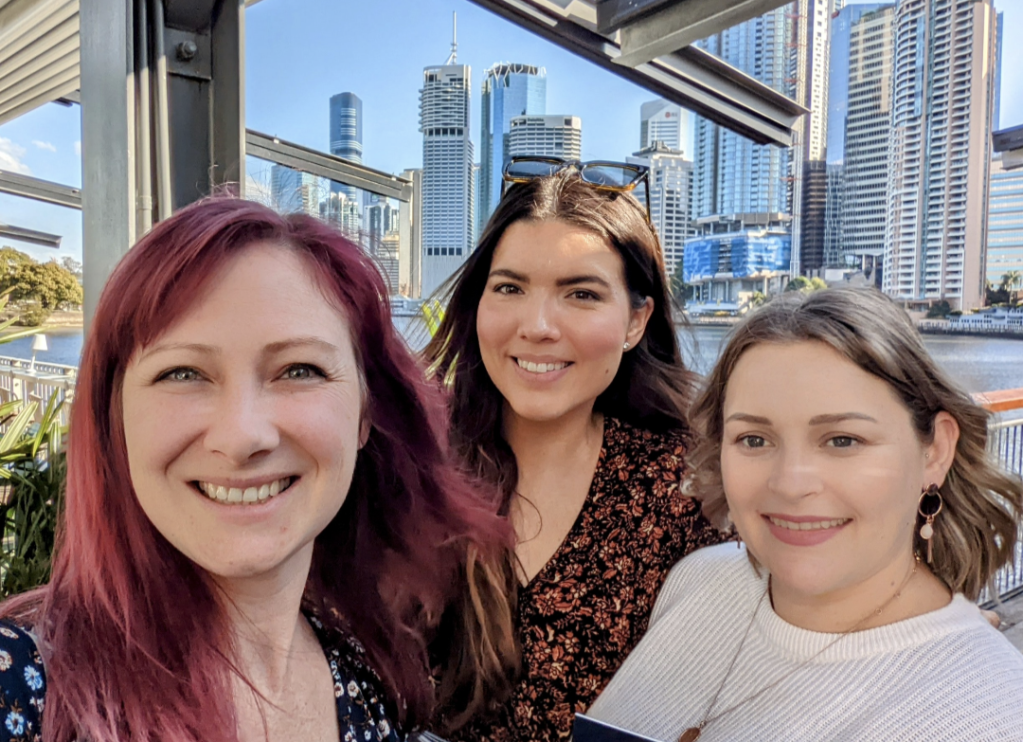 The Moore Moroney Consulting team smile into the camera. In the background is the Brisbane city skyline.